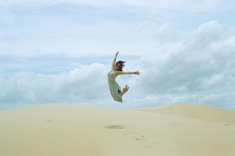 Sunlit Daytime: Woman in White Dress Playfully Leaping on Sandy Beach